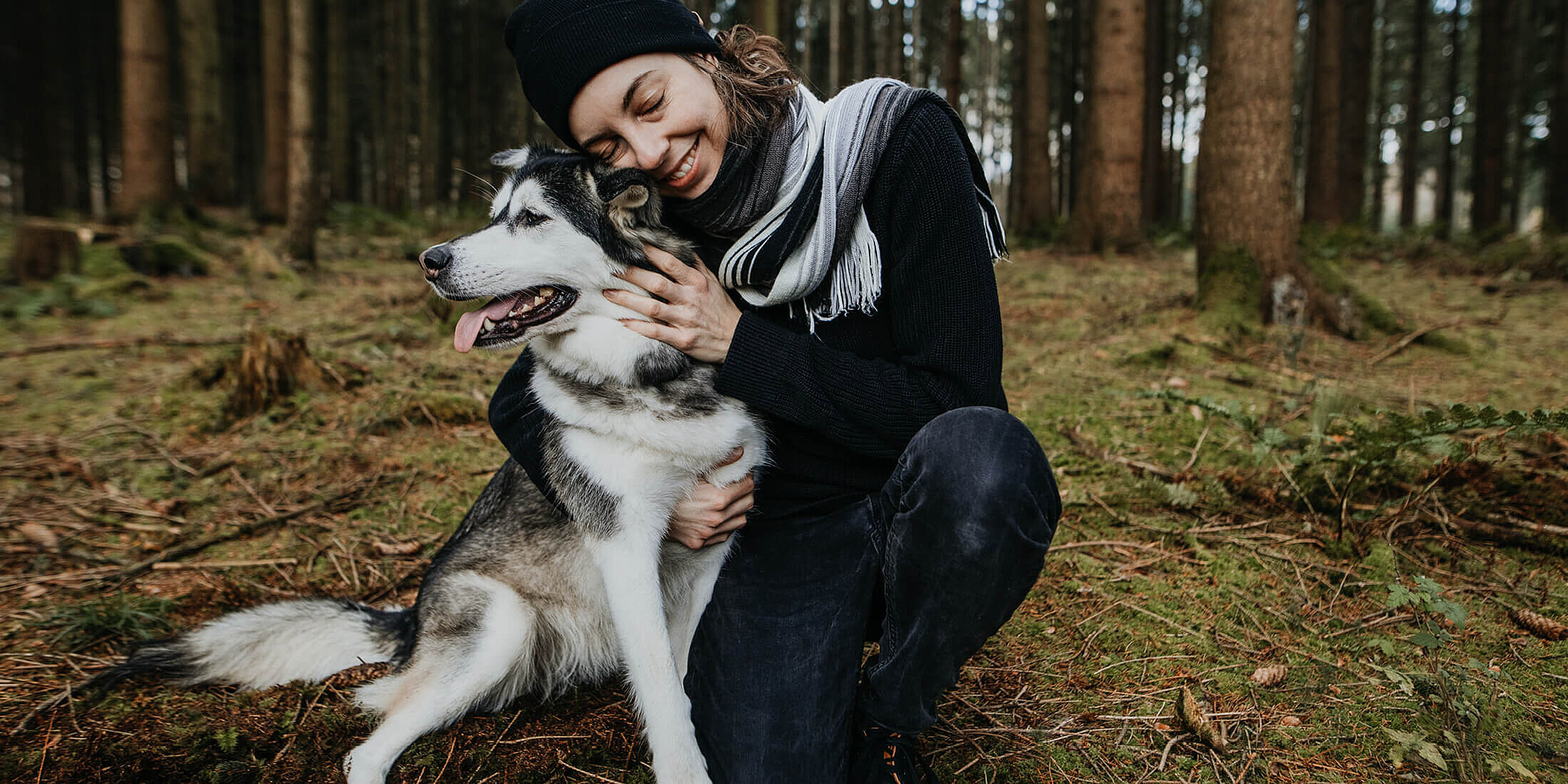 Eine Frau, die im Wald ihren Hund umarmt