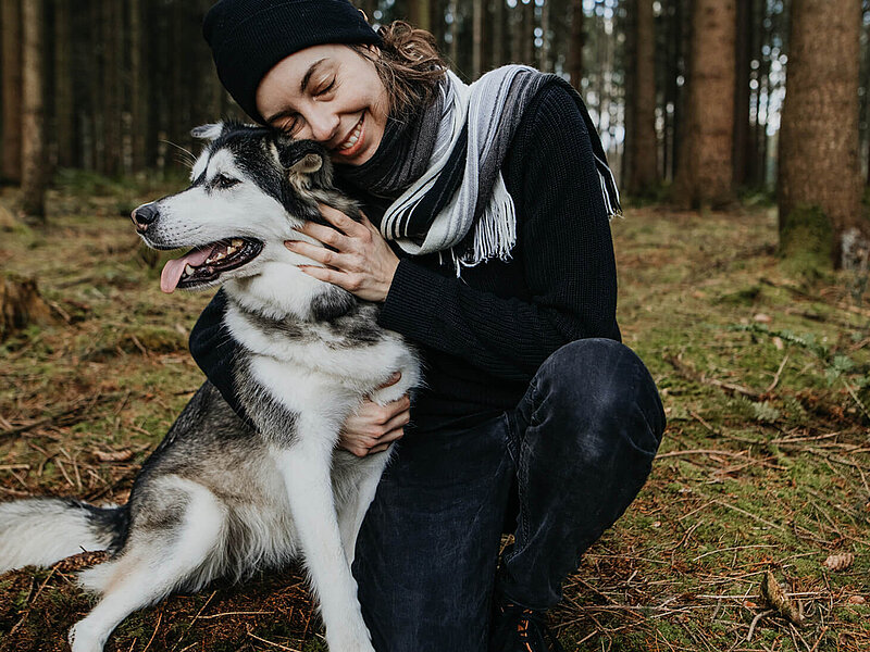 Eine Frau, die im Wald ihren Hund umarmt